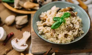 Kremowe risotto z grzybami, ozdobione listkiem bazylii. Pyszny ryż włoski w misce, otoczony świeżymi grzybami i papryczką chili.