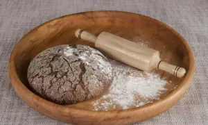 Drewniana miska z bochenkiem chleba, wałkiem i mąką. Czy pszenica durum ma gluten? Tak, zawiera go.