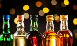 Rząd pięciu butelek z różnymi alkoholami, w tym zielona z niebieskim korkiem, przezroczysta z pomarańczowym, zielona z czarnym, przezroczysta ze złotym i przezroczysta z kolejnym złotym. Tło rozmyte, z ciepłymi, okrągłymi światłami. Idealne na wieczór ...