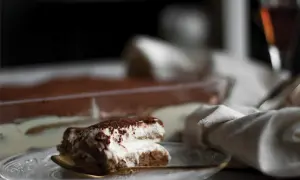 Pyszne tiramisu na talerzyku, z widocznym w tle deserem w naczyniu. Zastanawiasz się, jaki alkohol do tiramisu?