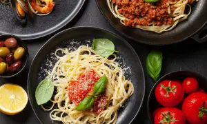 Pyszne spaghetti z sosem pomidorowym, posypane startym serem, obok krewetki z małżami, mięso mielone i świeże pomidory.