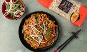 Gotowy do przygotowania dania z makaronem chow mein, który jest idealny do ramen. Na talerzu danie z warzywami i mięsem, obok miseczka kiełków i opakowanie makaronu.