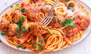 Pyszny makaron spaghetti z dziurką, polany sosem pomidorowym i posypany parmezanem, z soczystymi klopsikami.