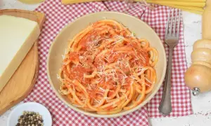 Pyszne bucatini amatriciana z pomidorowym sosem i parmezanem, obok kawałek sera i pieprz.