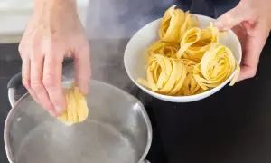 Ręce wkładają tagliatelle do wrzącej wody. Kluczowe jest, ile wody do makaronu, by był idealny.