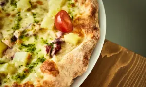 Pyszna pizza z kawałkami ananasa, ośmiornicy i pomidorkiem, obficie posypana zielonym pesto i roztopioną **mozzarellą w bloku**.