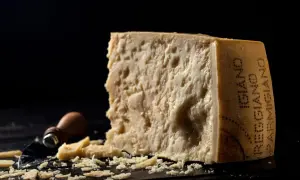 Kawałek parmezanu, którego inna nazwa to Grana Padano, z widocznymi kryształkami i okruchem sera obok.