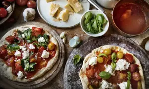 Dwie pizze z sosem pomidorowym, świeżymi pomidorkami, bazylią i kremową włoską mozzarellą. Obok składniki: parmezan, czosnek, pomidory.