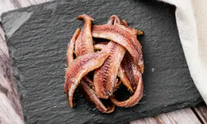 Kupa rybek anchois ułożona na czarnej desce, gotowa do podania.