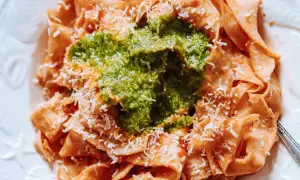 Pappardelle all'arrabbiata z zielonym pesto i parmezanem. Szerokie wstążki makaronu w sosie pomidorowym, przykryte intensywnym, zielonym pesto.