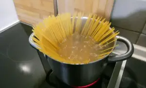 Długie spaghettoni gotują się w garnku na kuchence.