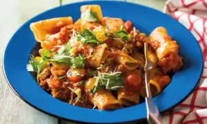Pyszne mezzi rigatoni w sosie pomidorowym z mięsem mielonym, pomidorkami koktajlowymi i świeżą natką pietruszki, podane na niebieskim talerzu.