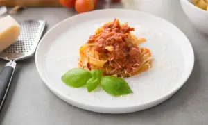 Talerz z makaronem tagliatelle polanym sosem pomidorowym, posypany parmezanem i udekorowany bazylią.