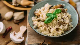 Kremowe risotto z grzybami, ozdobione listkiem bazylii. Pyszny ryż włoski w misce, otoczony świeżymi grzybami i papryczką chili.
