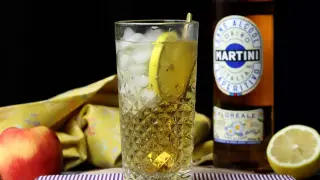 Orzeźwiający spritz bezalkoholowy z plasterkiem cytryny w szklance z lodem. Obok butelka Martini Floreale i jabłko.