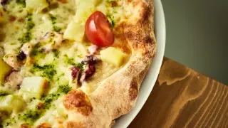 Pyszna pizza z kawałkami ananasa, ośmiornicy i pomidorkiem, obficie posypana zielonym pesto i roztopioną **mozzarellą w bloku**.