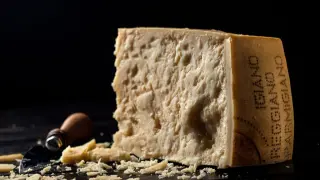 Kawałek parmezanu, którego inna nazwa to Grana Padano, z widocznymi kryształkami i okruchem sera obok.