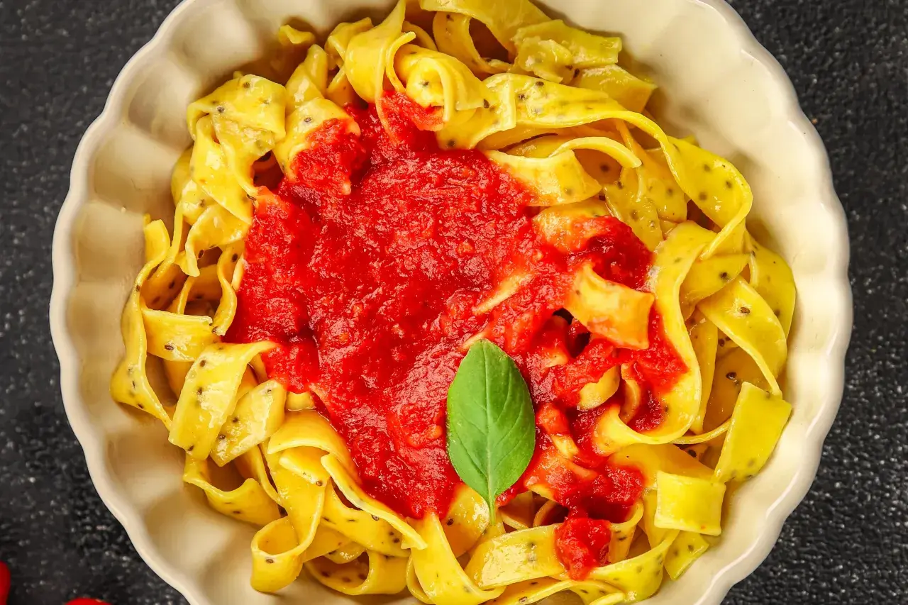 Pappardelle, czyli gruby makaron spaghetti, polane sosem pomidorowym i udekorowane listkiem bazylii.