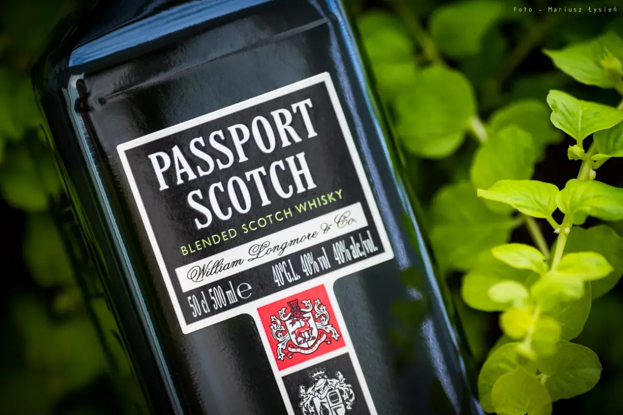 Butelka szkockiej whisky Passport Scotch, z zielonymi liśćmi w tle. Ten alkohol to idealny towarzysz podróży.