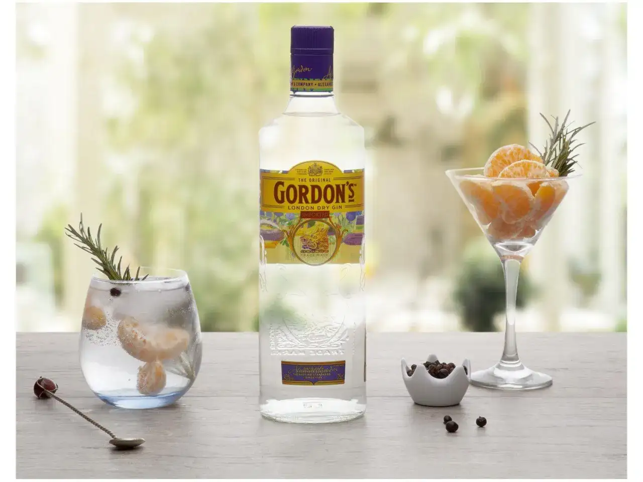 Gordon's alkohol: butelka ginu, drink z mandarynką i rozmarynem, kieliszek z mandarynką i rozmarynem, miseczka z jałowcem.