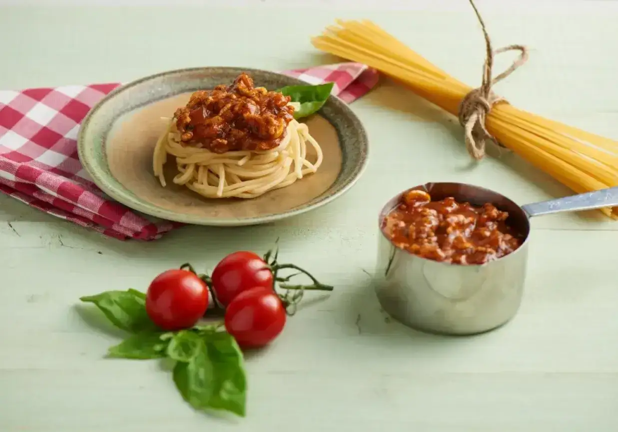 Pyszny sos do spaghetti z mięsem mielonym, podany na talerzu z makaronem, obok pomidorków i świeżej bazylii.