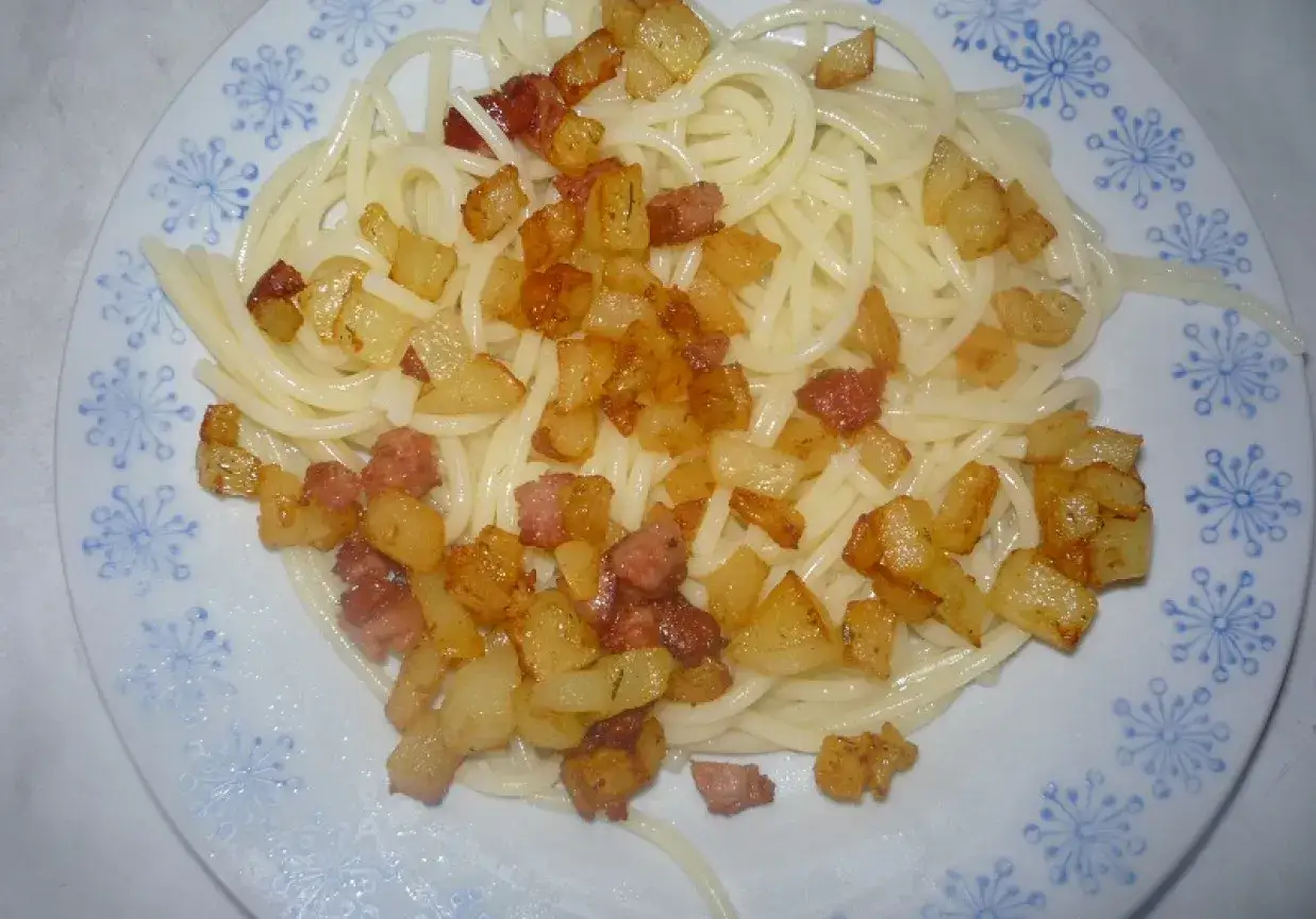 Makaron z ziemniakami i skwarkami, podany na talerzu z niebieskim wzorem.