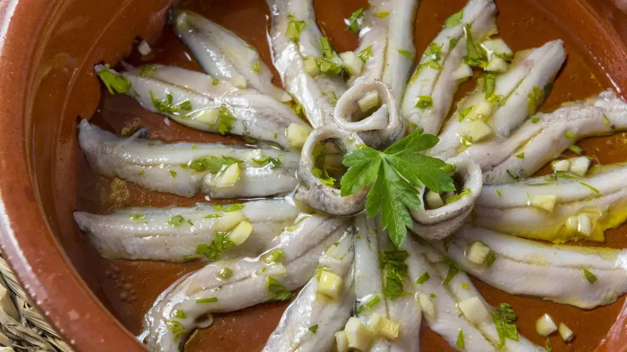Delikatne rybki anchois ułożone w okrąg, polane oliwą z oliwek, z czosnkiem i natką pietruszki.