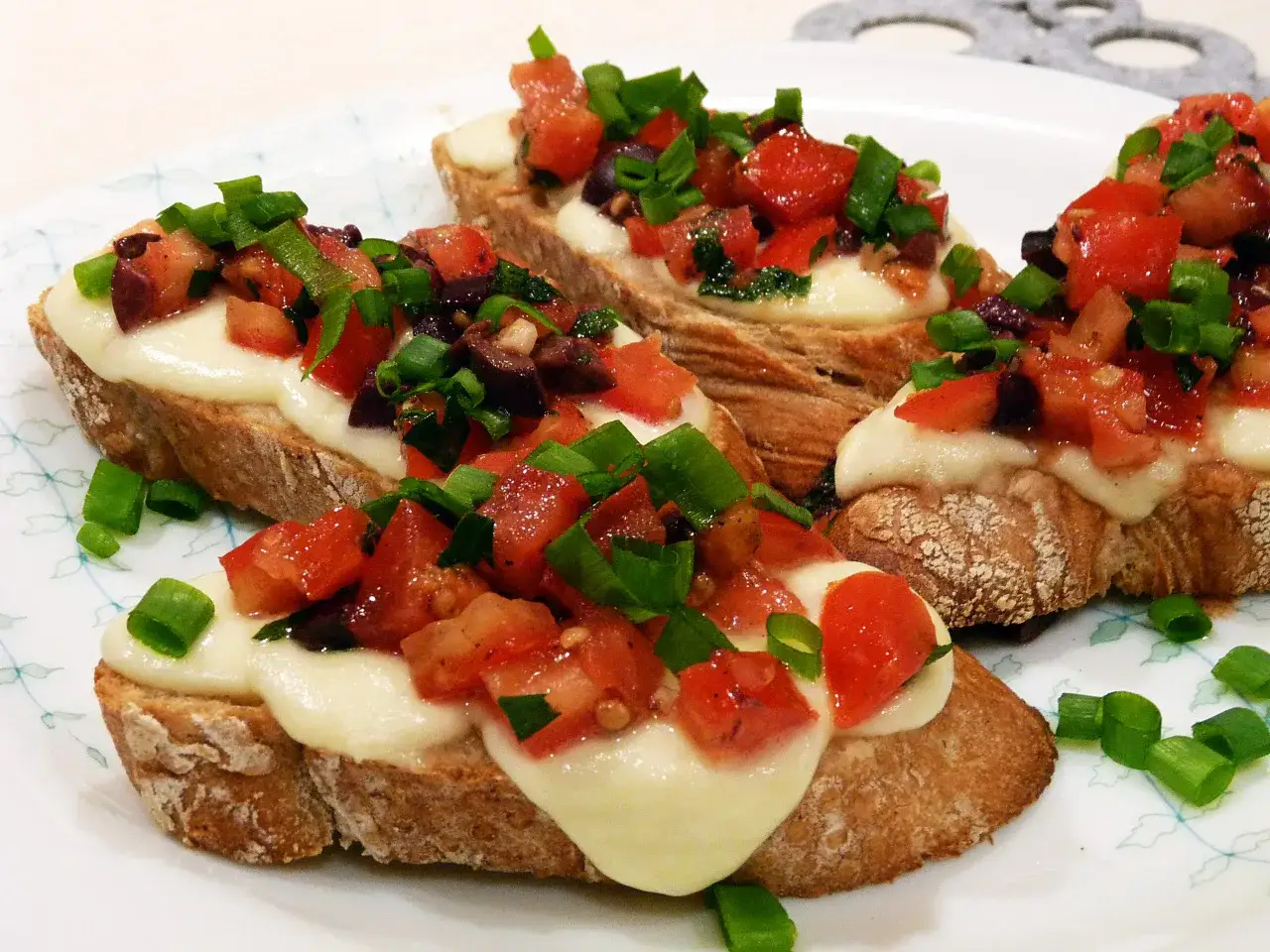 Bruschetta z pomidorami i mozzarellą: chrupiące pieczywo, roztopiony ser, świeże pomidory, oliwki i szczypiorek. Idealny przepis na szybką przekąskę.