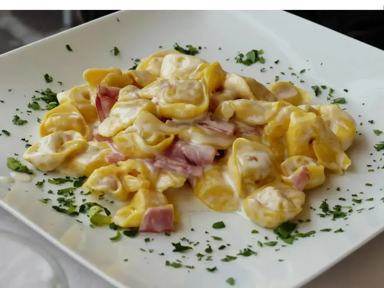Pyszne tortellini z mięsem w kremowym sosie, posypane świeżą natką pietruszki. Idealne na obiad.