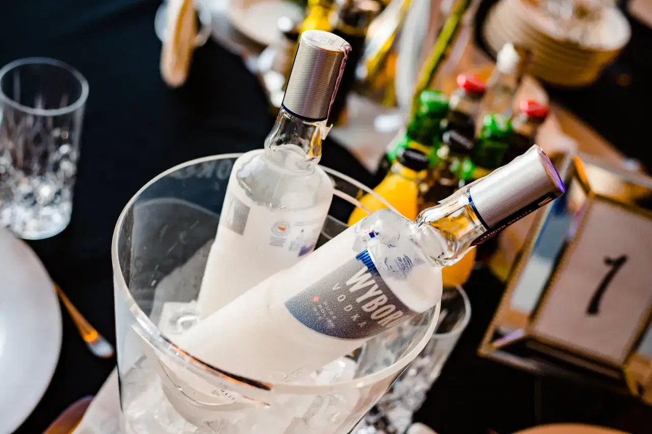Butelki Wyborowej w wiaderku z lodem, gotowe na toast. W tle inne napoje i dekoracje stołu, zapowiedź dobre alkohole.