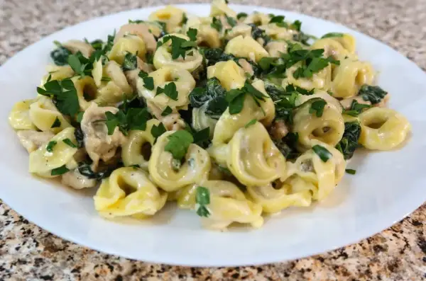 Tortellini z ricottą i szpinakiem w kremowym sosie, posypane natką pietruszki. Idealne danie, które można podawać samo lub z dodatkiem kurczaka.