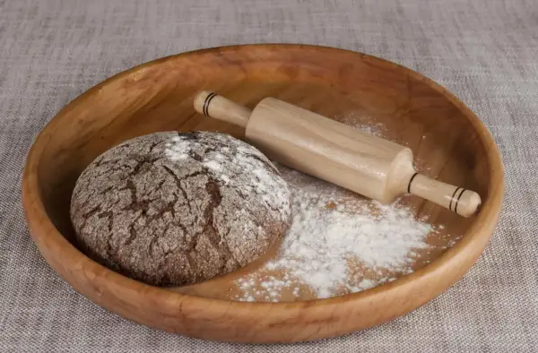 Drewniana miska z bochenkiem chleba, wałkiem i mąką. Czy pszenica durum ma gluten? Tak, zawiera go.