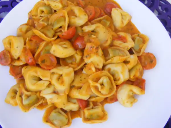 Pyszne tortellini ze szpinakiem w kremowym sosie pomidorowym z kawałkami pomidorków.