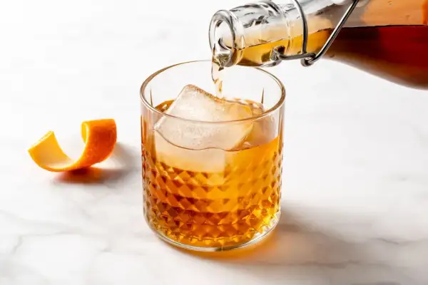Bursztynowy drink z lodem i skórką pomarańczy, nalewany z butelki. Czuć w nim subtelny smak amaretto.