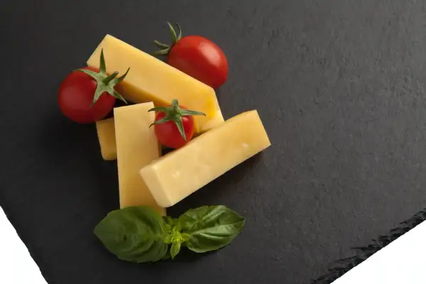 Kawałki żółtego sera, pomidorki koktajlowe i listki bazylii na czarnej desce. Czy to pecorino?