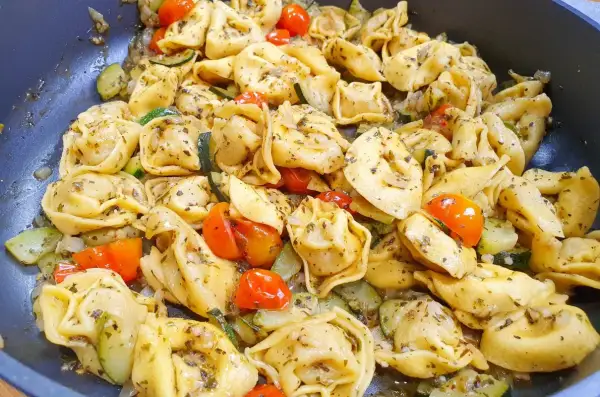 Pyszne tortellini z serem, podsmażane z cukinią i pomidorkami koktajlowymi, doprawione ziołami.