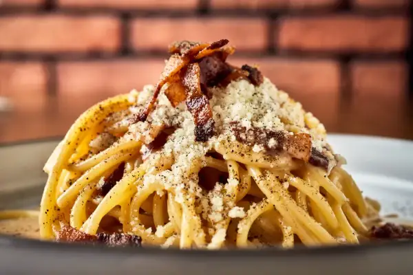 Pyszne spaghetti carbonara, klasyka włoskich przepisów na makaron, posypane parmezanem i chrupiącym boczkiem.