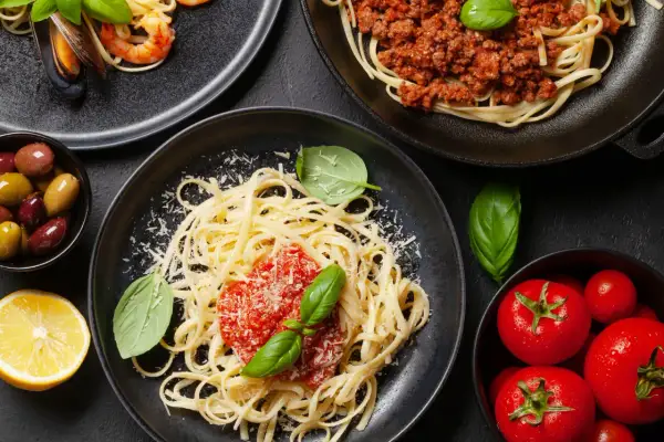 Pyszne spaghetti z sosem pomidorowym, posypane startym serem, obok krewetki z małżami, mięso mielone i świeże pomidory.