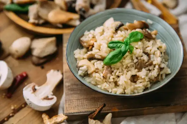 Kremowe risotto z grzybami, ozdobione listkiem bazylii. Idealny ryż do risotto, który wchłonął smak leśnych skarbów.