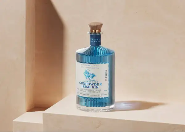 Elegancka butelka Drumshanbo Gunpowder Irish Gin, z niebieskim płynem i wytłoczonym jelonkiem, idealna na prezent dla miłośników ginów.