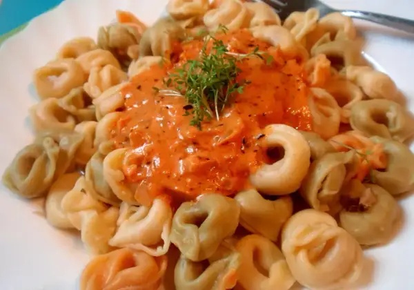 Kolorowe tortellini w kremowym sosie pomidorowym, udekorowane świeżą rukolą. Pyszny sos do tortellini kusi aromatem.