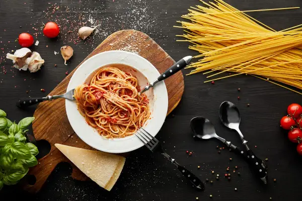 Talerz spaghetti z sosem pomidorowym, czosnek, pomidory, bazylia i parmezan. Takie składniki sugerują, skąd pochodzi spaghetti.