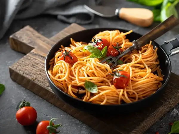 Szybki obiad z makaronem spaghetti w sosie pomidorowym, udekorowany pomidorkami koktajlowymi i bazylią. Idealny na każdy dzień.