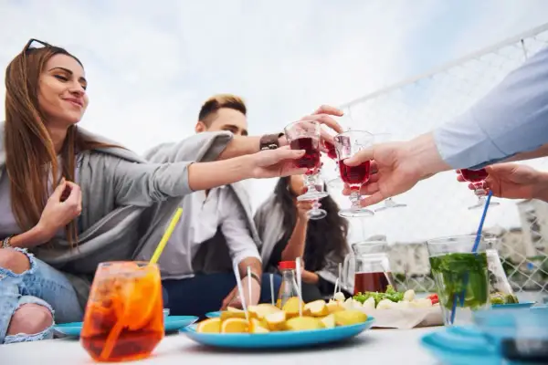 Grupa przyjaciół wznosi toast czerwonym aperitifem, ciesząc się spotkaniem na świeżym powietrzu.