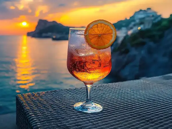Orzeźwiający drink z pomarańczą na tle zachodzącego słońca nad morzem. Idealny na wakacje, zastanawiasz się crodino co to? To włoski aperitif!