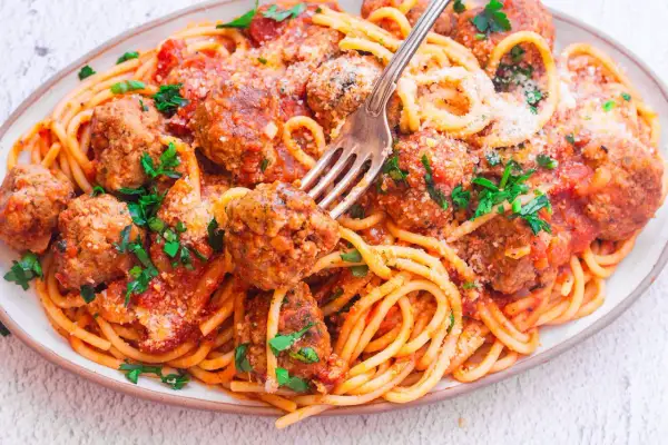Pyszny makaron spaghetti z dziurką, polany sosem pomidorowym i posypany parmezanem, z soczystymi klopsikami.