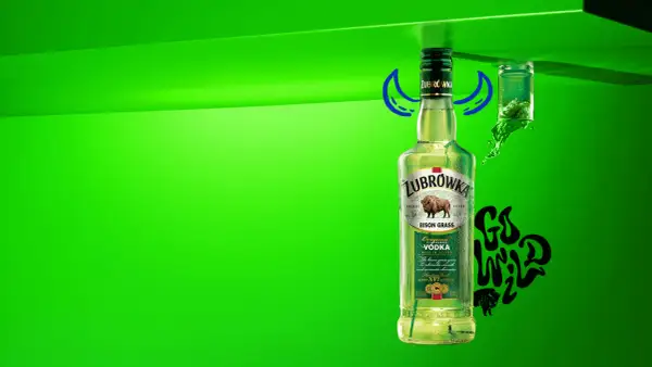 Butelka Żubrówki z trawą żubrową, 37,5% alkoholu. Obok kieliszek z zielonym płynem i napis "Go Wild".