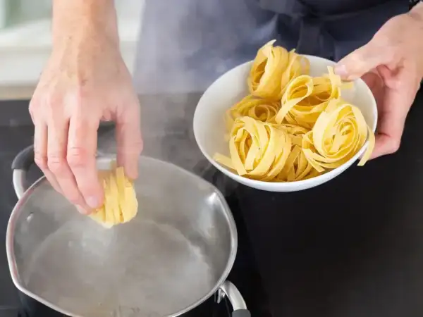 Ręce wkładają tagliatelle do wrzącej wody. Kluczowe jest, ile wody do makaronu, by był idealny.