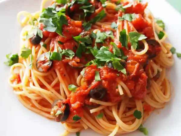 Pyszny makaron spaghetti z sosem pomidorowym, oliwkami i natką pietruszki. Czy makaron do spaghetti się płucze? Zazwyczaj nie, aby sos lepiej przylegał.