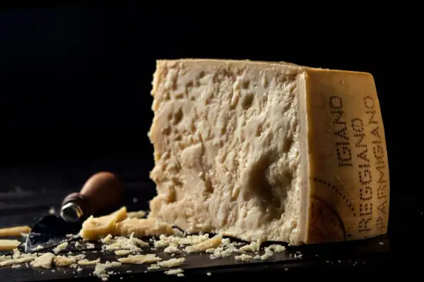 Kawałek parmezanu, którego inna nazwa to Grana Padano, z widocznymi kryształkami i okruchem sera obok.